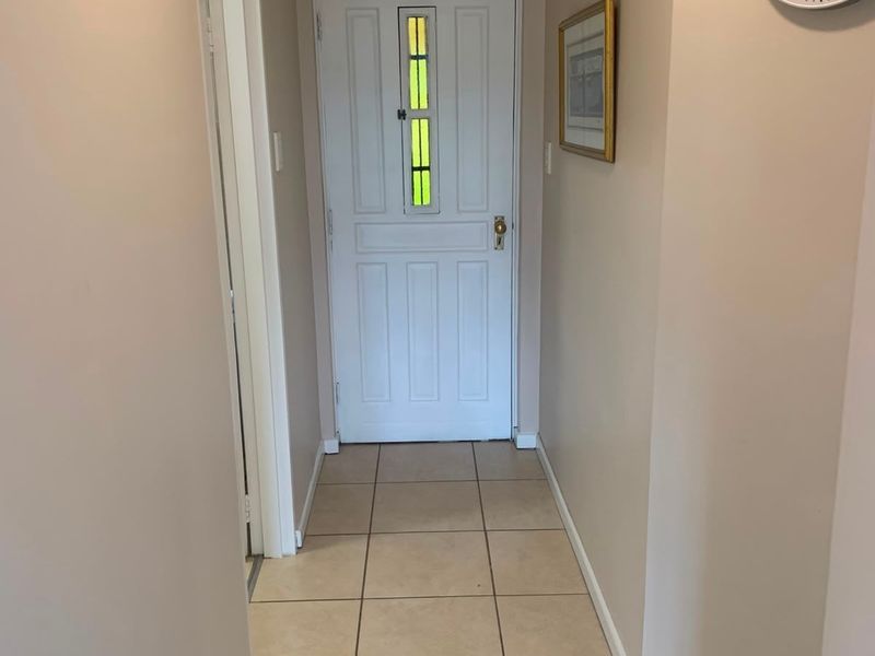A clean and functional hallway featuring neutral wall tones, tiled flooring, and a classic panelled front door with a decorative glass insert.