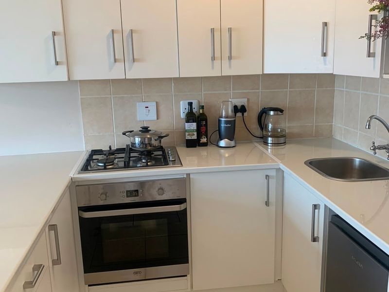 A compact, functional kitchen featuring white cabinetry, stone countertops, a gas hob, built-in oven, and neutral tiled backsplash and flooring.