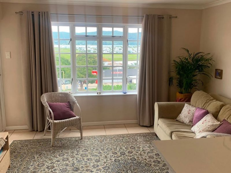 A bright living room featuring tiled flooring, a large multi-pane window with scenic views, and a glass-panelled door leading to an outdoor area.