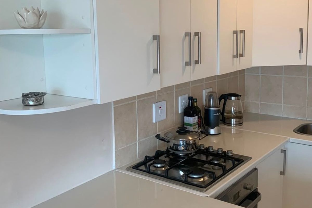 A functional kitchen featuring white cabinetry, stone countertops, a gas hob, built-in oven, and a tiled backsplash with a stainless steel sink.