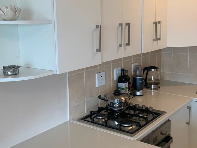 A functional kitchen featuring white cabinetry, stone countertops, a gas hob, built-in oven, and a tiled backsplash with a stainless steel sink.