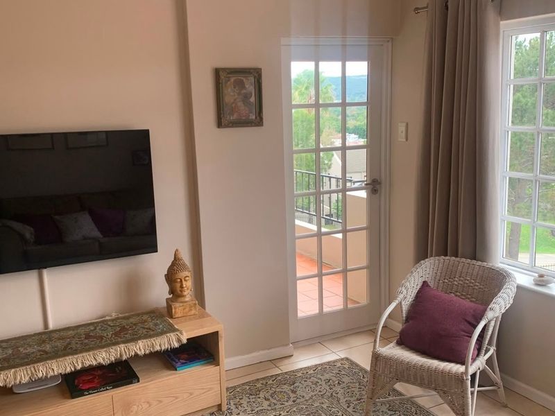 A bright living room featuring tiled flooring, a glass-paned french door leading to a balcony, and large mullioned windows with natural light.