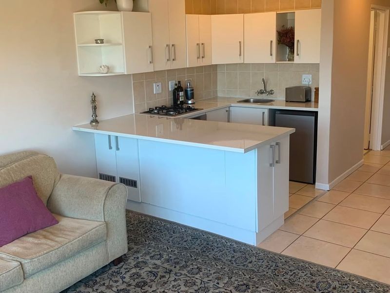 Compact open-plan kitchen featuring white cabinetry, stone countertops, a gas hob, and tiled splashback, seamlessly integrated with the living area.