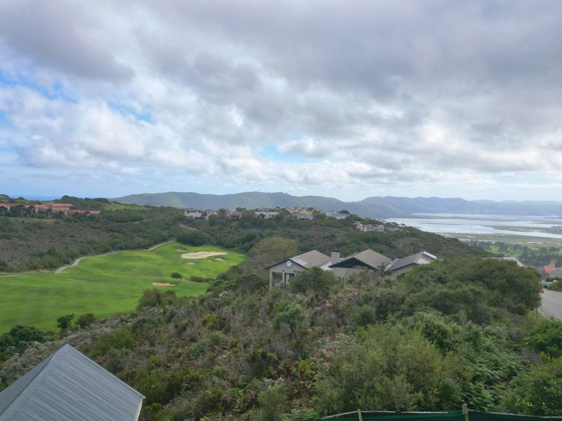 Elevated panoramic view overlooking a golf course, surrounding residential estate, and distant coastal landscape under a cloudy sky.
