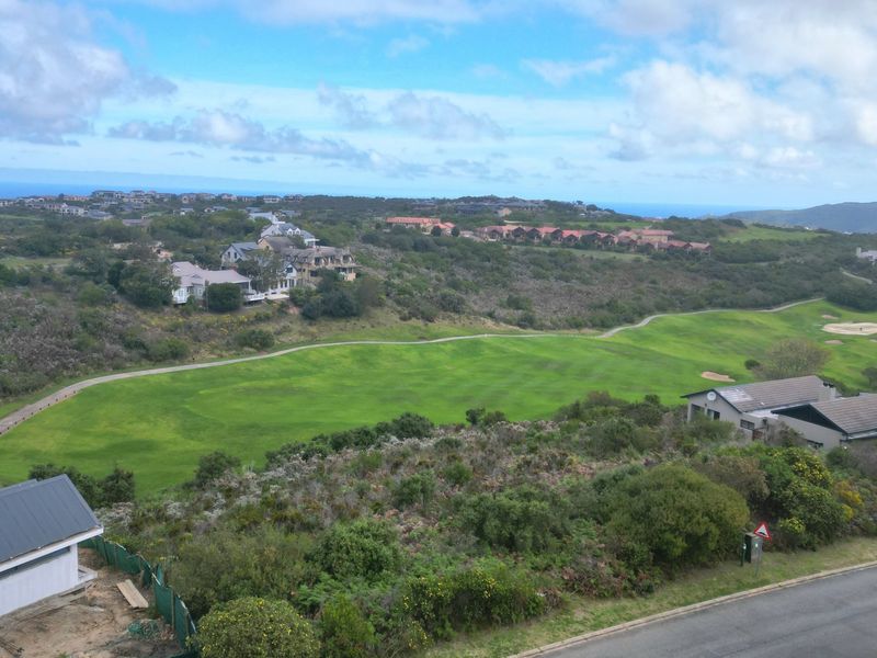 An elevated aerial view of a residential estate featuring a golf course, surrounding natural vegetation, and distant coastal scenery.