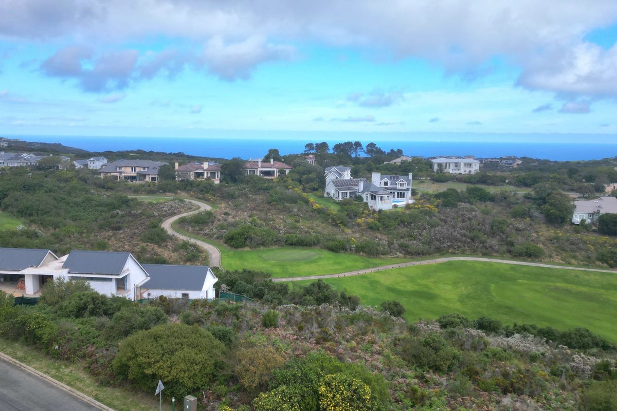 An aerial view of a residential estate featuring landscaped golf course grounds, paved pathways, and surrounding coastal scenery.