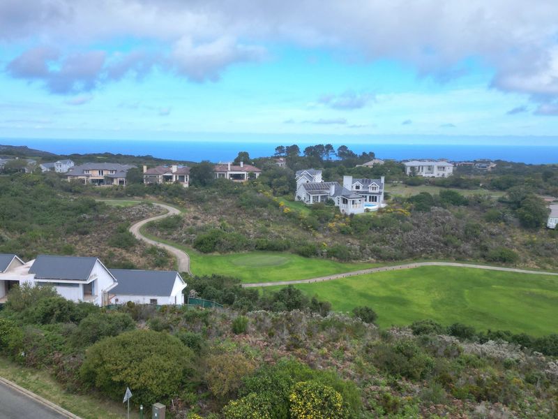 An aerial view of a residential estate featuring landscaped golf course grounds, paved pathways, and surrounding coastal scenery.
