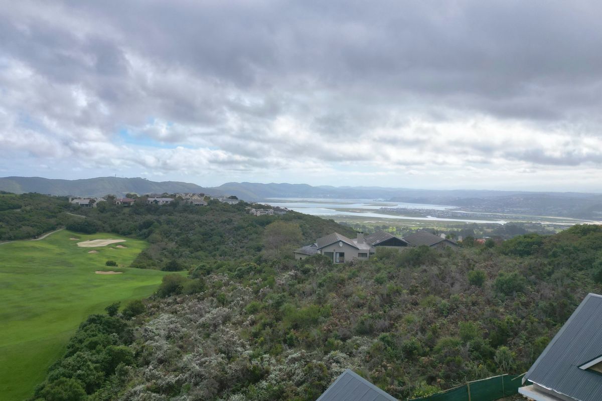 Elevated panoramic view overlooking a golf course, natural coastal vegetation, and a distant estuary under a cloudy sky.