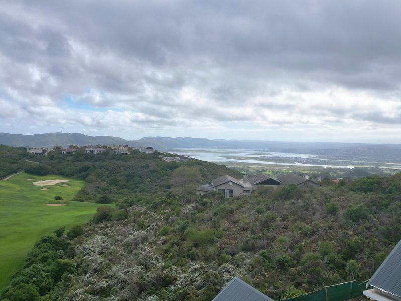 Elevated panoramic view overlooking a golf course, natural coastal vegetation, and a distant estuary under a cloudy sky.