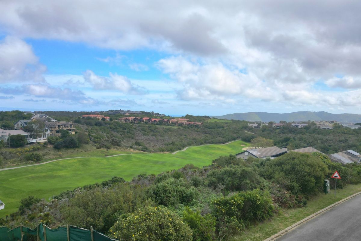An elevated view overlooking a lush green golf course and surrounding residential estate landscape under a cloudy sky.