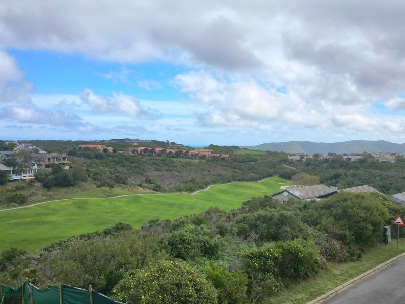 An elevated view overlooking a lush green golf course and surrounding residential estate landscape under a cloudy sky.