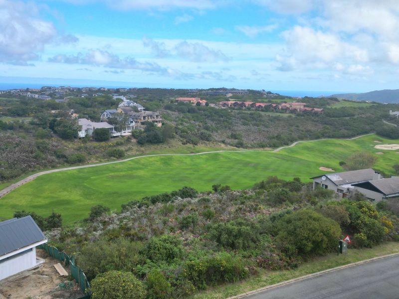 An elevated aerial view of a residential estate featuring a golf course, surrounding natural vegetation, and distant coastal scenery.