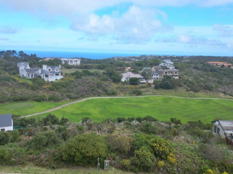 An aerial view of a residential estate featuring a golf course, surrounding natural vegetation, and distant ocean views.