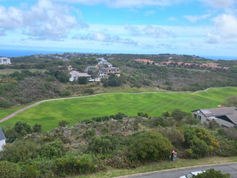 A scenic elevated view overlooking a lush green golf course with surrounding residential properties and distant coastal scenery.