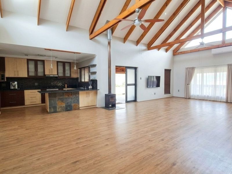 Spacious open-plan living area featuring vaulted timber beam ceilings, laminate flooring, a modern kitchen with stone island, and a cozy freestanding fireplace.