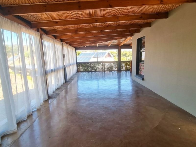 A spacious covered patio featuring polished concrete floors, exposed timber beam ceilings, and large glass sliding doors, offering a versatile outdoor living area.