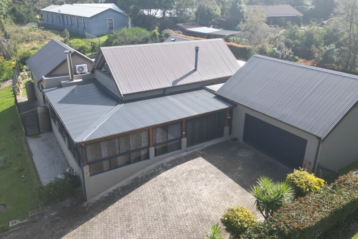 Aerial view of the property featuring a modern corrugated metal roof, paved driveway, double garage, and a covered patio area.