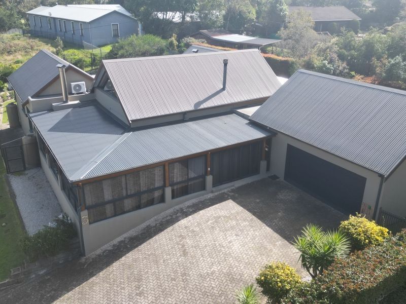 Aerial view of the property featuring a modern corrugated metal roof, paved driveway, double garage, and a covered patio area.