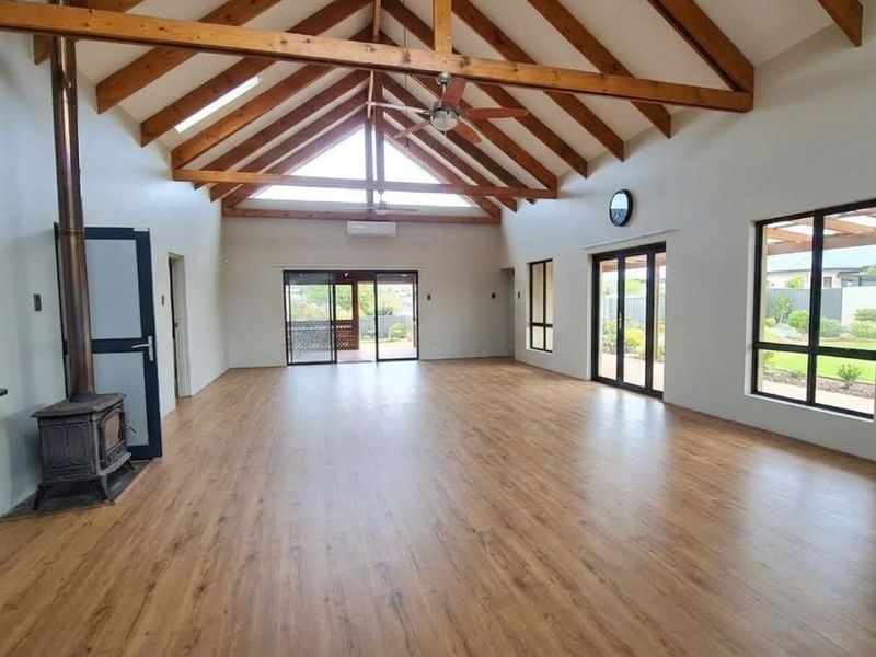 Spacious open-plan living area featuring a vaulted ceiling with exposed timber rafters, wood-burning fireplace, and large sliding doors leading to the garden.