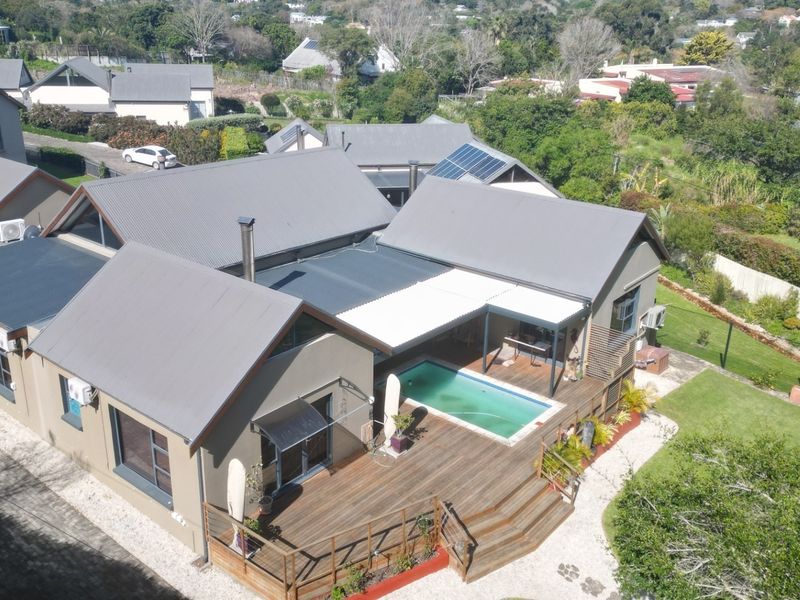 Aerial view of a residential property featuring a metal roof, timber decking, and an integrated swimming pool with a covered patio area.