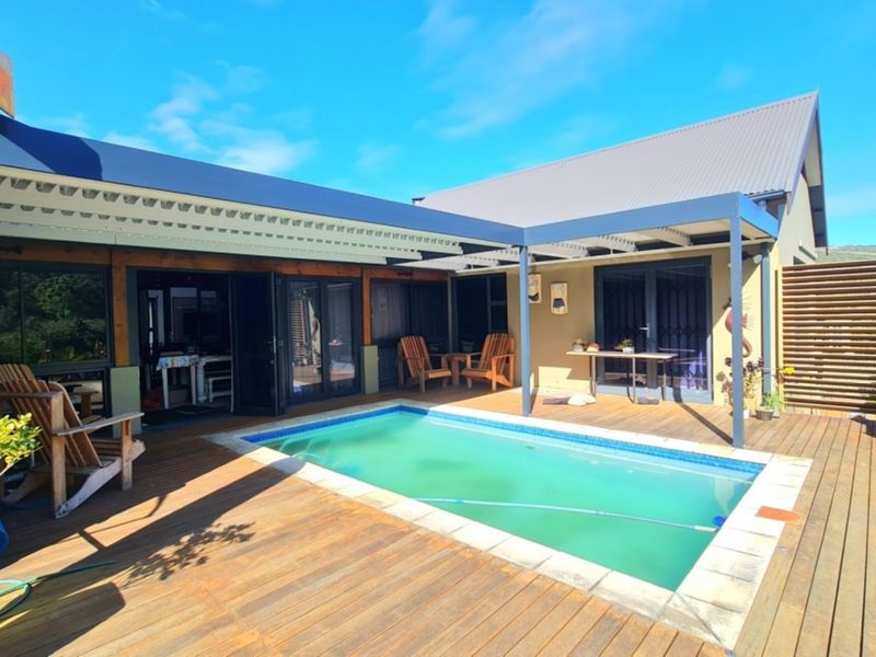 Outdoor pool area featuring timber decking, a covered patio structure, and direct access to the home through sliding glass doors.