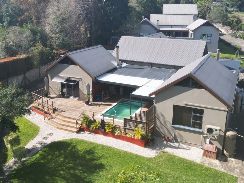 Aerial view of a residential property featuring a corrugated metal roof, timber decking, swimming pool, and landscaped garden area.