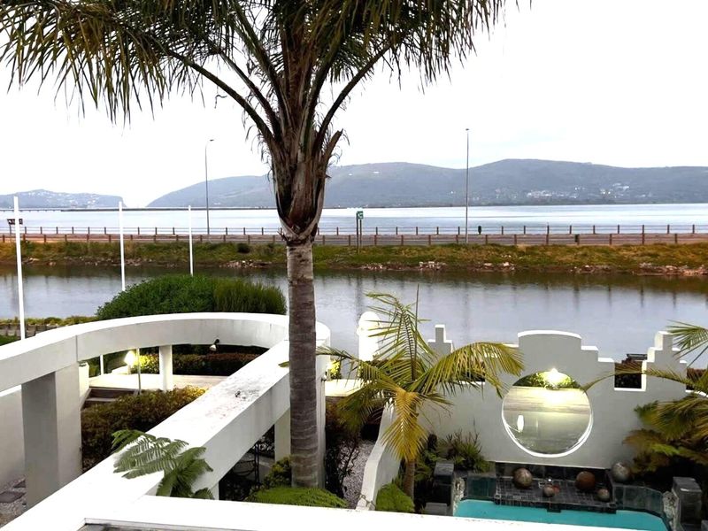 Elevated view overlooking a private swimming pool, landscaped garden, and a scenic waterfront with mountain vistas in the background.