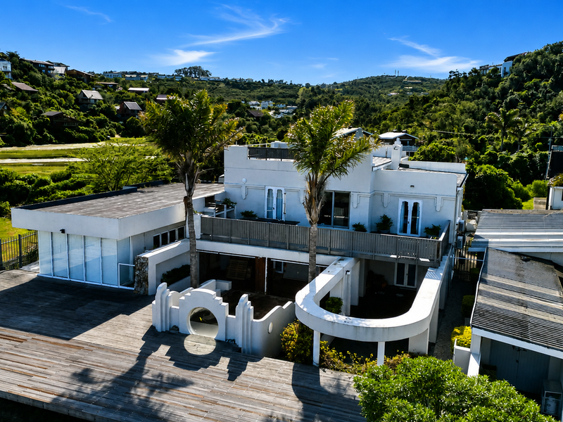 Aerial view of a multi-level residence featuring extensive timber decking, a balcony, and unique architectural parapet detailing set against a hillside landscape.