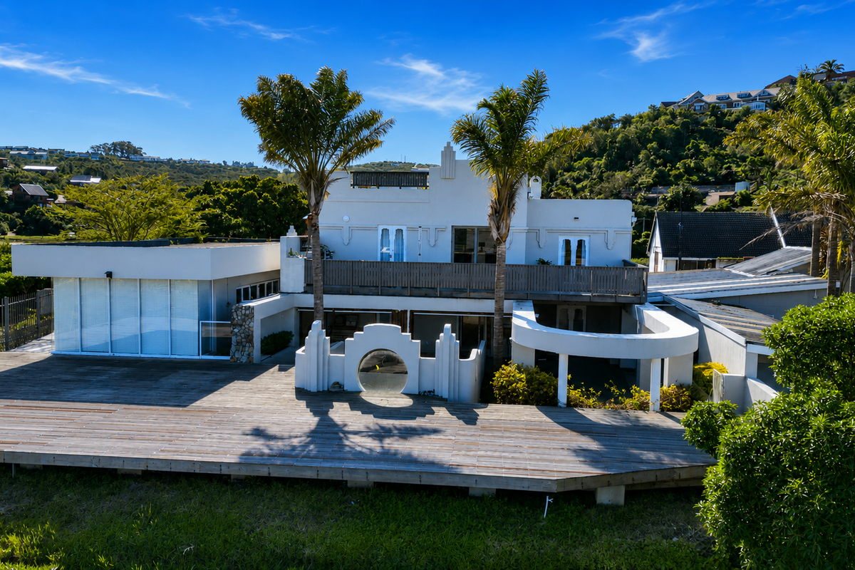 Rear view of a multi-level residence featuring extensive timber decking, a balcony, and unique architectural curved design elements set against a hillside backdrop.