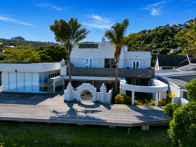 Rear view of a multi-level residence featuring extensive timber decking, a balcony, and unique architectural curved design elements set against a hillside backdrop.