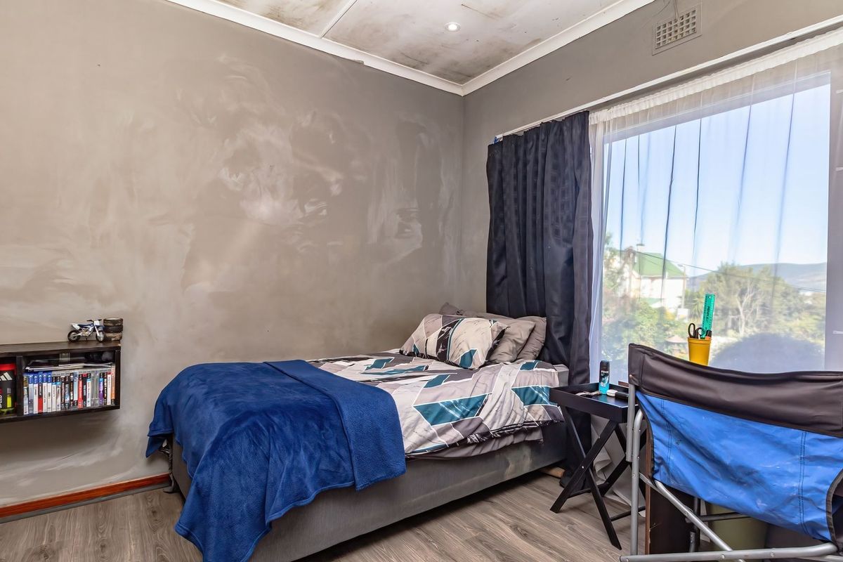 A bedroom featuring laminate flooring, a large window with security bars, and a built-in wall shelf, showing signs of ceiling water damage.