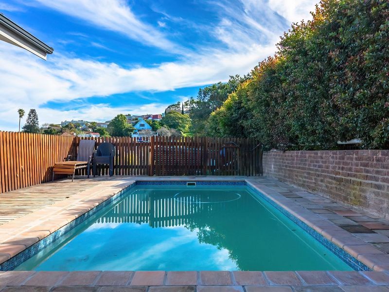 Outdoor pool area featuring a swimming pool, timber decking, and a brick retaining wall, enclosed by a timber picket fence.
