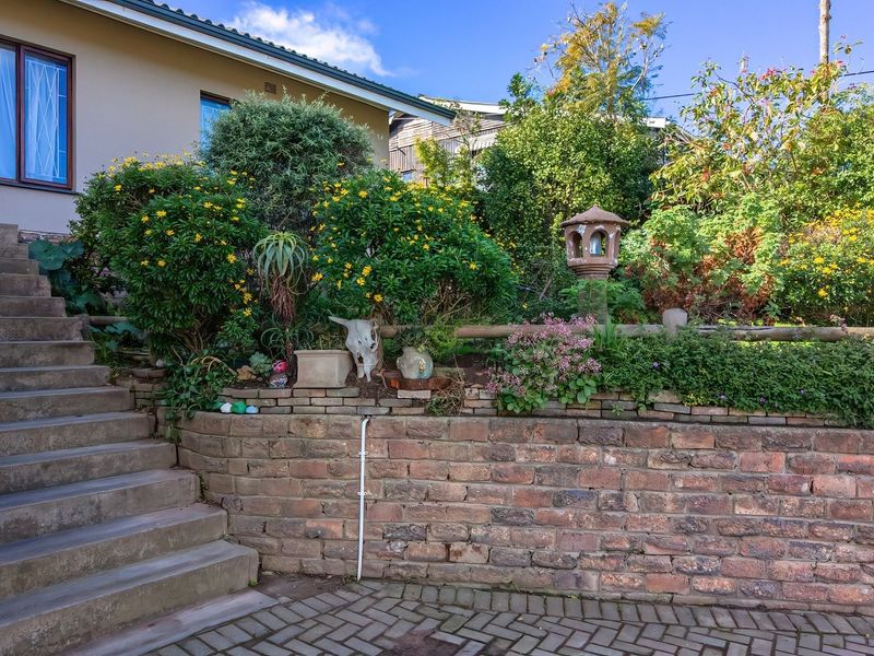 Front exterior view featuring a brick retaining wall, concrete staircase leading to the entrance, and established garden landscaping.