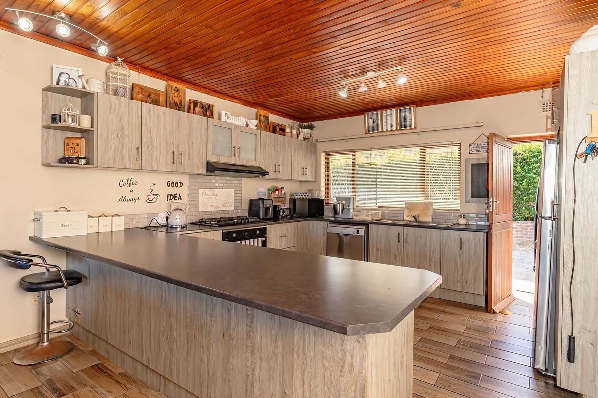 A functional kitchen featuring light wood-grain cabinetry, dark laminate countertops, a breakfast bar, and a distinctive timber-paneled ceiling with integrated lighting.