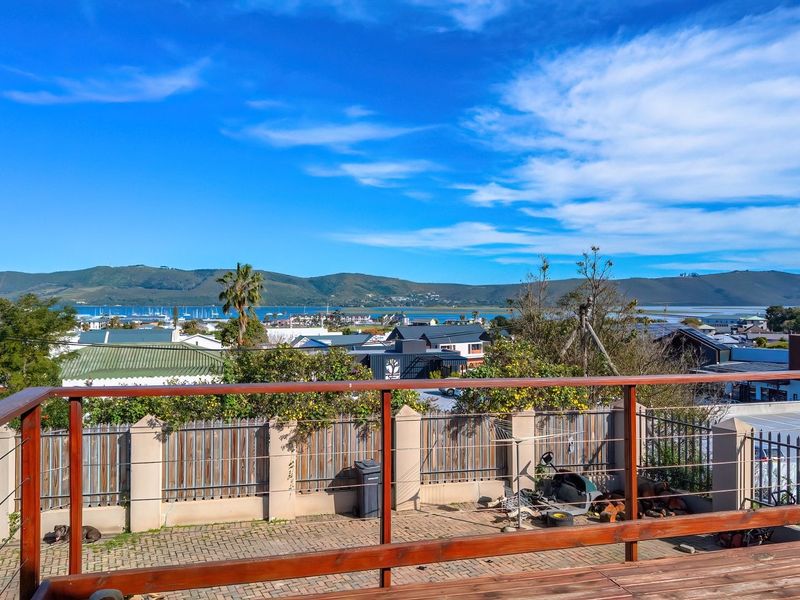 Elevated view overlooking the surrounding neighborhood, coastal landscape, and mountains from a wooden deck with a paved patio area below.