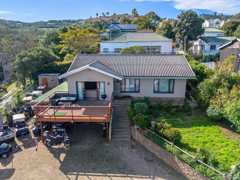 Aerial view of the rear elevation featuring a raised timber deck, paved driveway, and landscaped garden area.