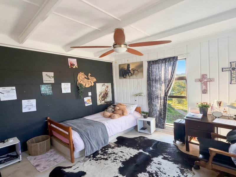 A bright bedroom featuring a vaulted ceiling with exposed beams, a ceiling fan, and a large window providing natural light and scenic views.
