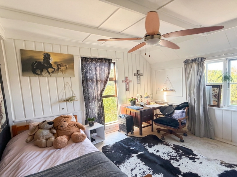 A bedroom featuring timber wall paneling, a ceiling fan, and large windows that provide natural light.