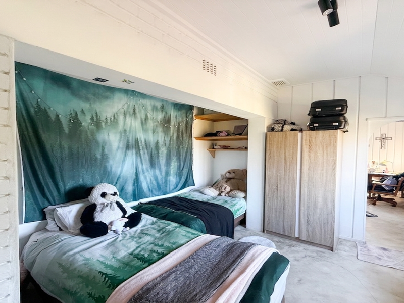 A bedroom featuring exposed brickwork, timber panelled walls and ceiling, and a built-in shelving alcove, leading through an archway to an adjacent room.