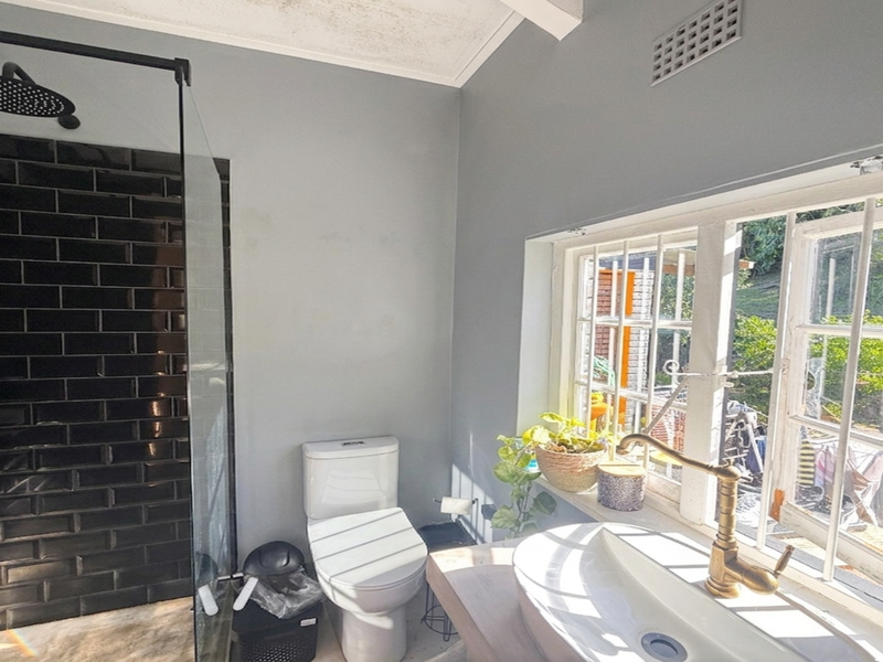 A bathroom featuring a black subway-tiled walk-in shower, a vessel sink with a brass faucet, and a window with security bars.