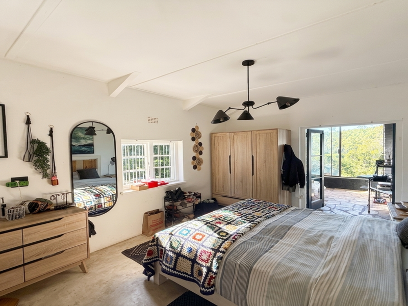 A bright bedroom featuring exposed ceiling beams, a built-in wardrobe, and a glass sliding door providing direct access to an outdoor patio area.