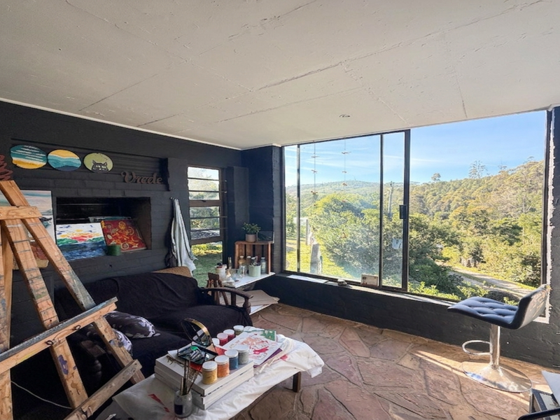 A sunlit living space featuring rustic stone flooring, dark painted brick walls, and a large window offering expansive views of the surrounding landscape.