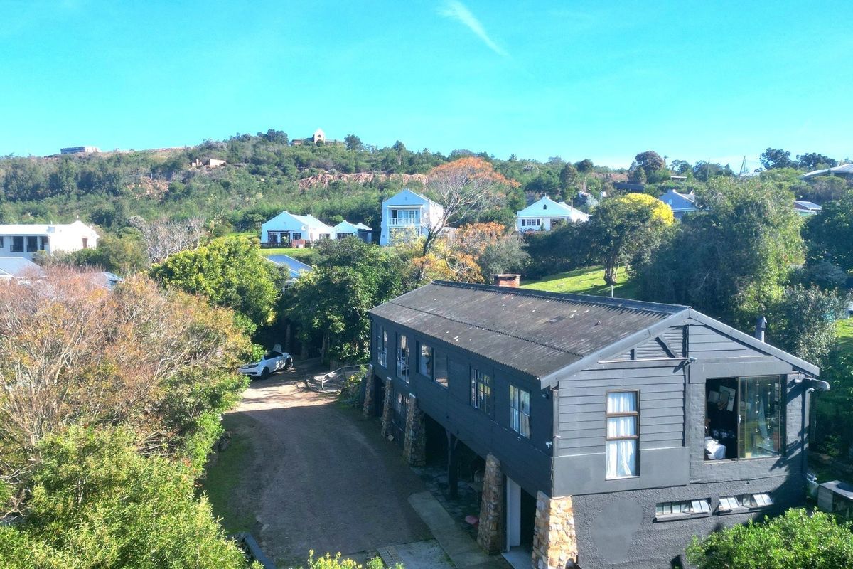 Aerial view of a two-story residential property featuring dark timber cladding, stone masonry supports, and a corrugated metal roof set in a hillside landscape.