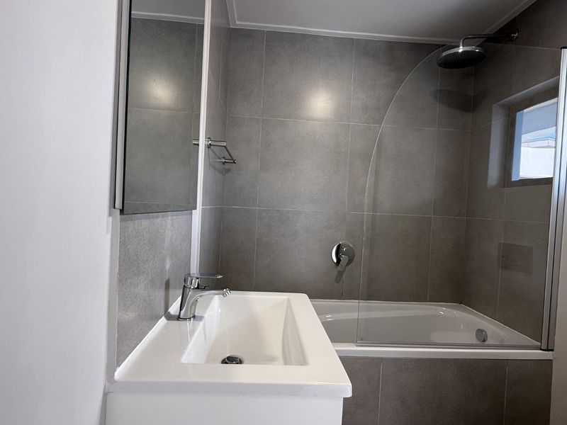 Modern bathroom featuring a sleek vanity, tiled walls, and a combined bathtub and shower with a glass screen.