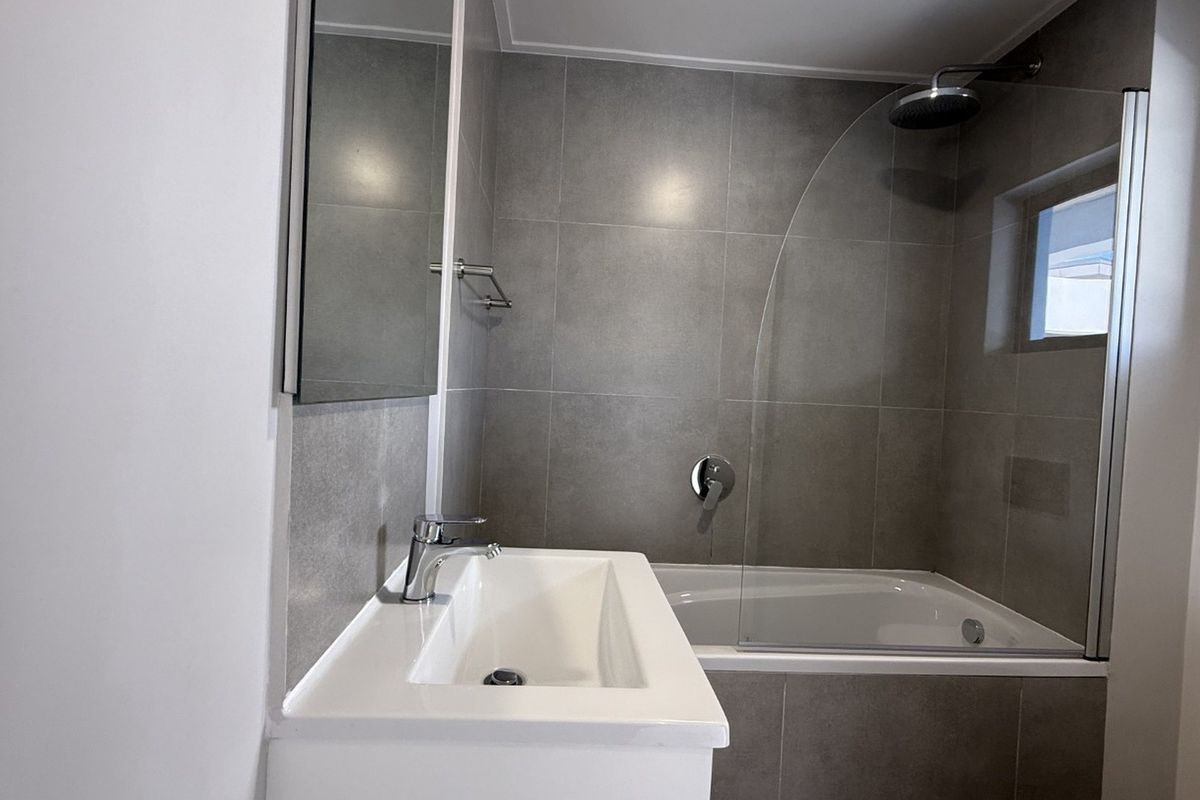 Modern bathroom featuring a sleek vanity, tiled walls, and a combined bathtub and shower with a glass screen.