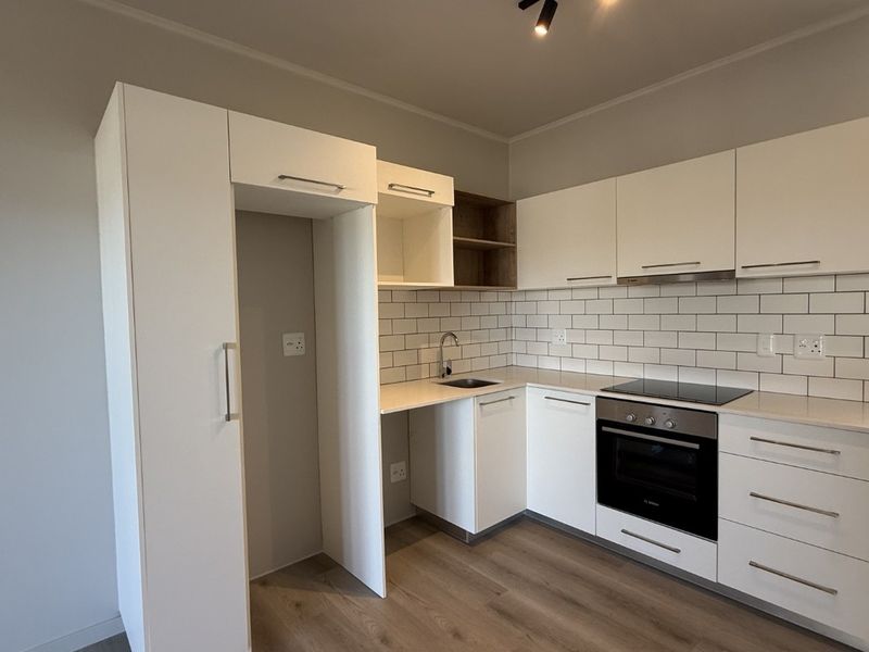 Modern kitchen featuring white cabinetry, subway tile backsplash, integrated oven and hob, and durable laminate flooring in a clean, contemporary layout.