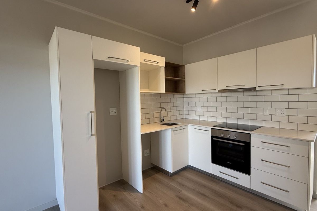 Modern kitchen featuring white cabinetry, subway tile backsplash, integrated oven and hob, and durable laminate flooring in a clean, contemporary layout.