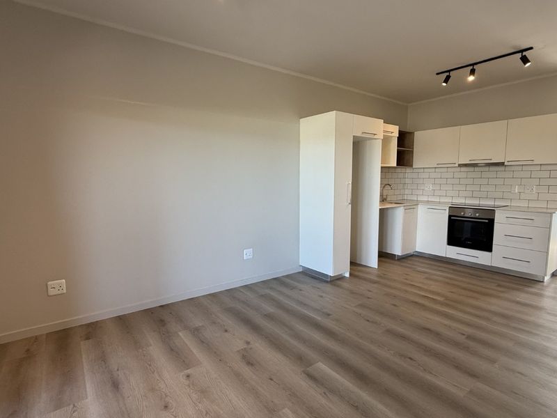 Modern open-plan living area featuring a sleek kitchen with built-in cabinetry, subway tile backsplash, integrated oven, and durable laminate flooring.