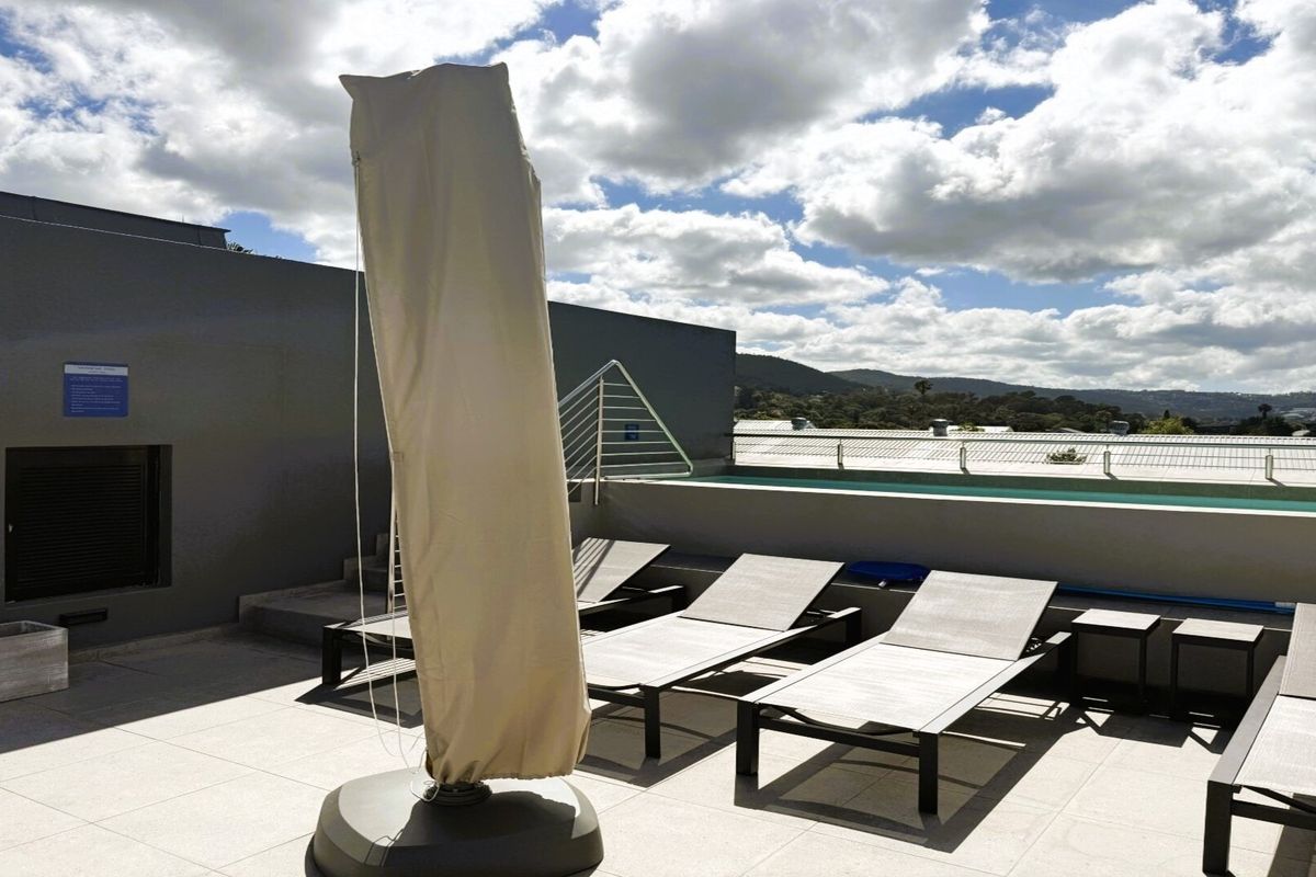 A rooftop pool area featuring a swimming pool, tiled flooring, and metal safety railings with scenic mountain views.