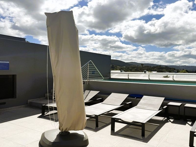 A rooftop pool area featuring a swimming pool, tiled flooring, and metal safety railings with scenic mountain views.